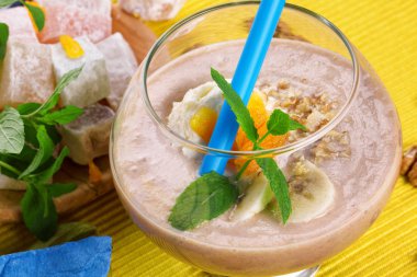 Nane, kayısı ve sarı kumaş zemin üzerine mavi pipet ile soğuk milkshake şeffaf bir bardak close-up. Parlak, tatlı Lokum ve meyveli içecek. Kokteyller için yaz partileri