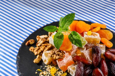 Bir karanlık cam levha lokum, rahat lokum veya Türk Lokumu, kahverengi tarihi meyve, ceviz ve nane özlü canlı yaprakları üzerinde çizgili bir arka plan üzerinde çizgili bir masa örtüsü closeup. Tatlılar kavramı.