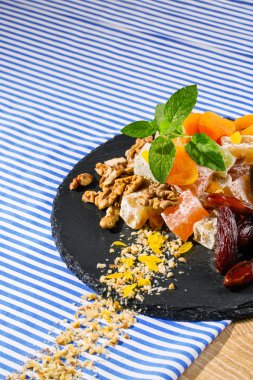 Türk Lokumu, lokum veya rahat lokum tarihi meyve, ceviz ve canlı taze nane yapraklarda çizgili bir masa örtüsü çizgili bir arka plan üzerinde siyah bir tabakta closeup. Tatlılar kavramı. Kopya alanı.