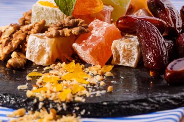 Tatlılar kavramı. Uzay kopyalayın. Bir tabak lokum, rahat lokum veya Türk Lokumu, kahverengi tarihi meyve, ceviz ve nane çizgili bir masa örtüsü ve karanlık bir plaka ile yakın çekim.