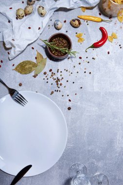 Öğle Yemeği malzemeler ve sofra takımı en iyi görünümü gri bir arka plan üzerinde. Bıldırcın yumurtası yanında baharat, defne yaprağı, parlak pul biber ve baharat ahşap kase yağ geçirmez kağıt üzerinde. Natürmort.