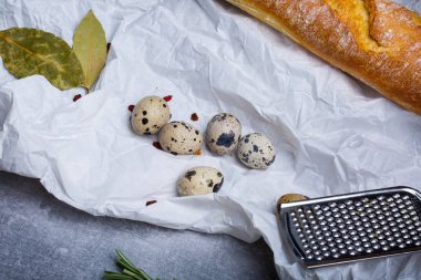Öğle Yemeği malzemeler beyaz yağ geçirmez kağıt arka plan üzerinde bir dizi bir görüntüyü yukarıdan. Beyaz baget, bıldırcın yumurtası, defne yaprağı ve metal rende. Gıda kavramı. Doğal taze ürünler.