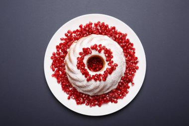 Üstten Görünüm şeker tozu sosu, kırmızı nar taneleri ve aromatik nane yaprakları ile beyaz mermer kek. Ev yapımı kek mor bir arka plan üzerine bir tabak. Klasik pasta tarifleri kavramı.