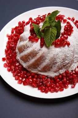 Üstten Görünüm şeker tozu sosu, kırmızı nar taneleri ve aromatik nane yaprakları ile beyaz mermer kek. Ev yapımı kek mor bir arka plan üzerine bir tabak. Klasik pasta tarifleri kavramı.