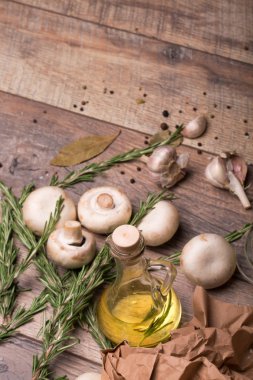 Rustik ahşap arka plan üzerinde beyaz champignon mantar görünümü top. Baharatlı sarımsak ampuller, yeşil biberiye yaprakları, baharat ve besleyici yağ bir tabloda bir cam şişe. Sağlıklı yemek hazırlığı. 