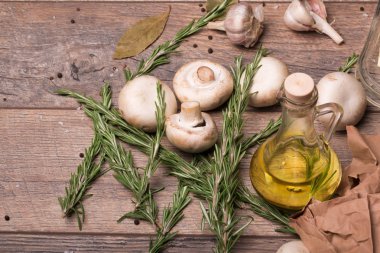 Rustik ahşap arka plan üzerinde beyaz champignon mantar görünümü top. Baharatlı sarımsak ampuller, yeşil biberiye yaprakları, baharat ve besleyici yağ bir tabloda bir cam şişe. Sağlıklı yemek hazırlığı. 