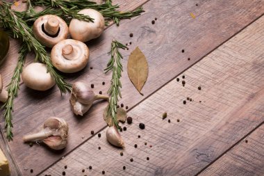 Rustik ahşap arka plan üzerinde beyaz champignon mantar görünümü top. Baharatlı sarımsak ampuller, yeşil biberiye yaprakları, baharat ve besleyici yağ bir tabloda bir cam şişe. Sağlıklı yemek hazırlığı. 