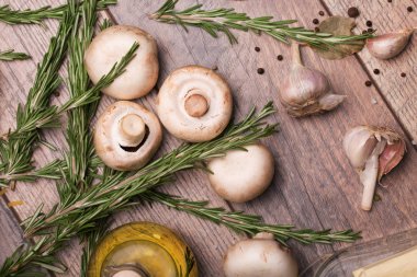 Rustik ahşap arka plan üzerinde beyaz champignon mantar görünümü top. Baharatlı sarımsak ampuller, yeşil biberiye yaprakları, baharat ve besleyici yağ bir tabloda bir cam şişe. Sağlıklı yemek hazırlığı. 