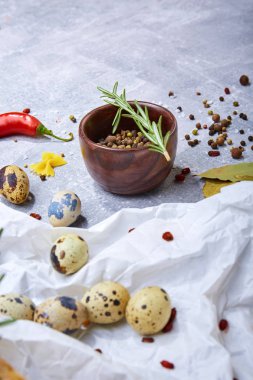 Beyaz bir kumaş ve bir kahverengi kase baharatlı siyah biber hafif bir taş zemin üzerine küçük bıldırcın yumurtası. Çeşitli Baharatlar: kırmızı biber, biber ve yeşil biberiye yaprağı. Protein yemek hazırlama.