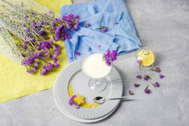 Gümüş kaşık ve parlak sarı carambola beyaz tabaklar, sarı ve mavi peçeteler, besleyici süt, küçük mor çiçekler ışık gri arka plan üzerinde grup içeren tablo