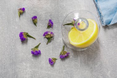 Mavi bir peçete, küçük mor çiçekler ve canlı sarı limon ile bir cam kap bir tabloyla closeup, turuncu ile hamuru vitamin dolu bir açık gri renkli, üstten görünüm ekşi.