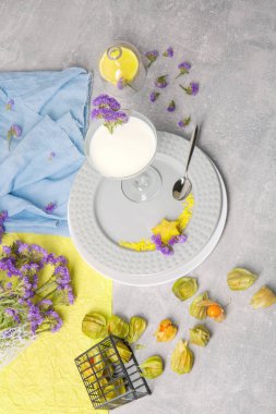 Gümüş kaşık ve parlak sarı carambola beyaz tabaklar, sarı ve mavi peçeteler, besleyici süt, küçük mor çiçekler ışık gri arka plan üzerinde grup içeren tablo