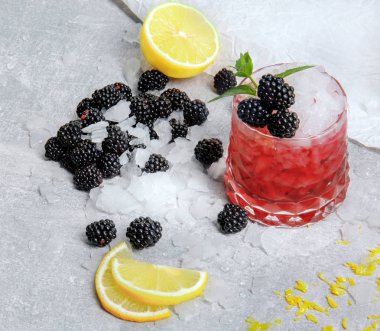 Geniş gözlük tam bir alkolik berry içecek baharatlı nane, limon dilimleri ve buz gibi beyaz masa arka plan üzerinde tatlı böğürtlen. Çilek ve turuncu yaz kokteyl serinletici.