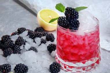 Geniş gözlük tam bir alkolik berry içecek baharatlı nane, limon dilimleri ve buz gibi beyaz masa arka plan üzerinde tatlı böğürtlen. Çilek ve turuncu yaz kokteyl serinletici.