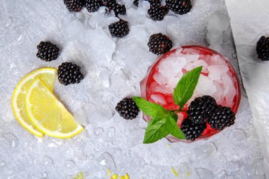 Dondurulmuş beyaz zemin üzerine bir bardak buz ve kırmızı meyve suyu ve meyve dolu bir manzara yukarıdan. Reçel, nane, limon limon ve böğürtlen ile kokteyl soğuk yakın çekim resim.