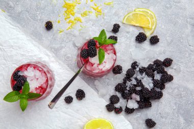 Birkaç süslü gözlük tam soğuk, buzlu içecek baharatlı nane, limon parçaları, sulu böğürtlen ve dondurulmuş beyaz masa arka plan üzerinde metal kaşık. Meyve ve çilek ile serinletici kokteyller.
