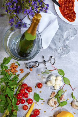 Beyaz bir tabak, kırmızı parlak domates, kuşkonmaz, sarımsak, badem, bir şişe şampanya, gümüş tirbuşon, yakın çekim ile bir tabak fasulye konserve. Küçük çiçekler, bıçak ve çatal gri bir arka plan üzerinde.