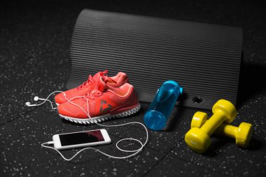 Sportif aksesuarlar, spor eğitim siyah bir arka plan üzerinde renkli bir dizi. Mavi sportif şişe, parlak turuncu Eğitim ayakkabı, sarı salak-bells, siyah pilates mat. Spor, eğitim kavramı.