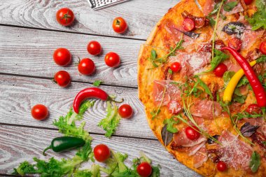 Taze yapılmış prosciutto pizza domates, biber ve salata ile yakın çekim bir resmini bırakır. Lezzetli İtalyan yemekleri bir ahşap masa arka plan üzerinde. İtalyan mutfağı. Pişirme kavramı.