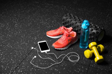 siyah streching mat, mavi sportif şişe, turuncu Eğitim ayakkabı, sarı salak-bells ve kulaklık ile modern telefon yakın çekim resim