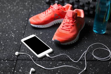 siyah streching mat, mavi sportif şişe, turuncu Eğitim ayakkabı, sarı salak-bells ve kulaklık ile modern telefon yakın çekim resim