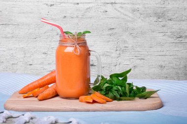 Sağlıklı yaz içecek bir mason kavanoza yenileniyor. Olgun havuç tüpler ve fesleğen yanında sulu bir kokteyl bir ahşap kesme masa üzerine bırakır. Detoks havuç içki saman üzerinde gri bir ahşap arka plan ile.