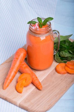 Bir mason kavanoza bir vitamin içeceği olgun havuç tüpler ve yeşil fesleğen yaprakları kesme masanın yanında dolu bir görünüm yukarıdan. Detoks içecek. Mavi kumaş arka plan üzerinde serinletici bir havuç yüzlü.