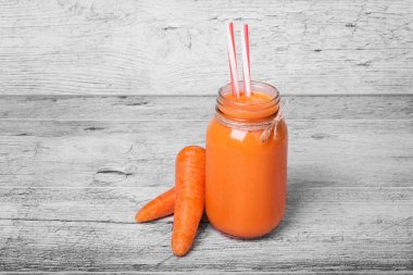 Bir bardak havuç milkshake veya saman açık ahşap arka planı üzerinde içme ile güler yüzlü yakın çekim. Taze havuç suyu iki tüm havuç ile bir şişe. Sebze kavramı.