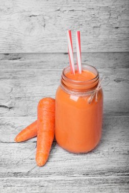 Gri bir ahşap arka plan üzerinde saman içme ile havuç milkshake ya da güler yüzlü dolu bir mason kavanoza yakın çekim. Taze havuç suyu iki tüm havuç ile bir şişe. Tatlı havuç suyu. Sebze kavramı.