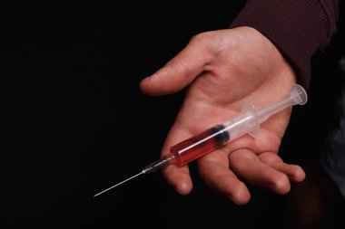 Bir adamın elini close-up bir şırınga bir doz eroin ile doymuş bir siyah arka plan üzerinde tutuyor. Narkotik kırmızı sıvı Hipodermik tam bir bağımlı. Uyuşturucu ve uyuşturucu kavramı.