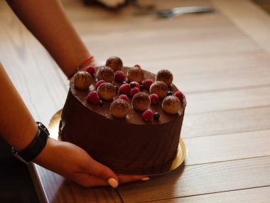 Bir tablo süngerimsi çikolatalı kek iştah açıcı özlü pembe Ahududu ve blackcurrants bir garsonun ellerini koymak. Bir şekerci bulanık bir açık renkli ahşap bir masaya koyar bir tatlı pasta.