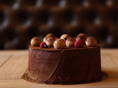 İştah açıcı çikolatalı pasta ile ışık ahşap bir masa ile kakao serpilir ve ahududu ve kahverengi bulanık arka plan üzerinde siyah kuş üzümü ile dekore edilmiş.