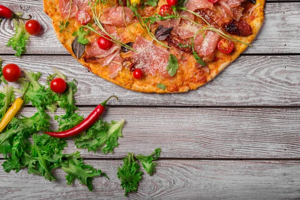 Delicious bright dish on a rustic wooden table background. A view from above on a tasty pepperoni pizza with red hot chili pepper and salad leaves. Italian cuisine. Cooking concept. Copy space.