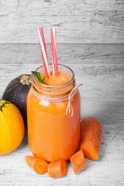 A tall bottle with a healthful detox beverage on a spacious gray table background. Chopped carrots and colorful zucchinis on a table. Orange juice with spicy mint for a liquid snack. Copy space.