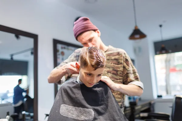 Kapper barbershop parihopher strechot kleine jongen zittend op een stoel — Stockfoto