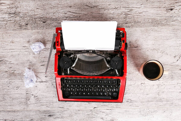 Печатная машинка красная с бумагой в ней и на столе
