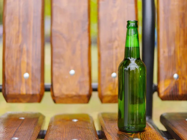 Uma garrafa de cerveja verde fica em um banco na rua — Fotografia de Stock