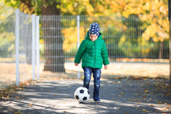 Menino brincando com uma bola no outono na rua — Fotografia de Stock