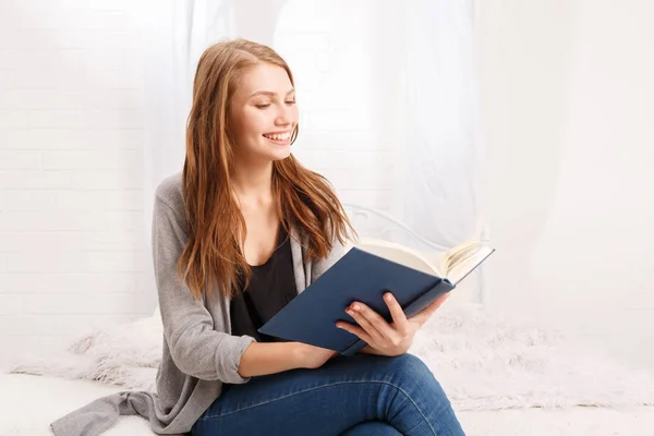 Счастливая девушка читает книгу с улыбкой — стоковое фото