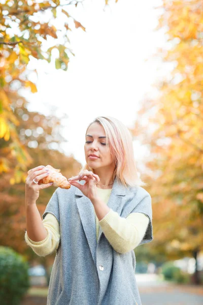 Una chica sostiene un croissant en su mano —  Fotos de Stock