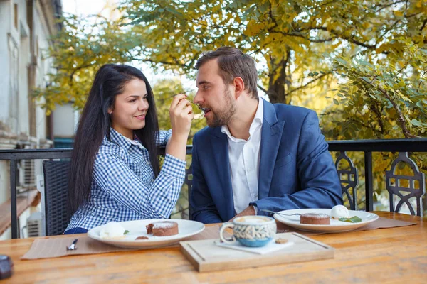 Young couple in love is sitting in cafe and woman is feeding cake her man. — Stock Photo, Image