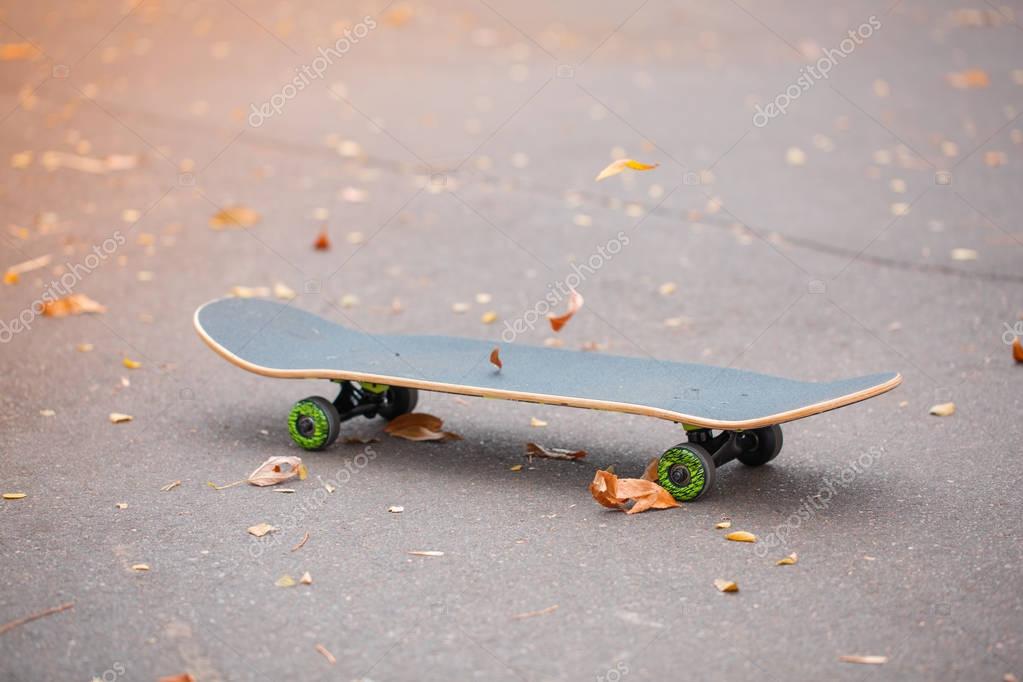 Modern gray skateboard lying on the road. Skate with green wheels for riding. Copy space. Close-up of skateboard. Sport concept.