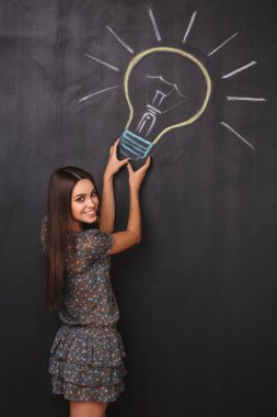 Çekici bir genç kız bir fikri vardır. Mutlu bir öğrenci yakınındaki tahtaya çizim ampul. Fikir kavramı yakalamak