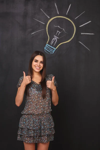 一个年轻的学生 靠近黑板上的灯泡 一位商界女性以竖起大拇指表示赞许的姿态 — 图库照片