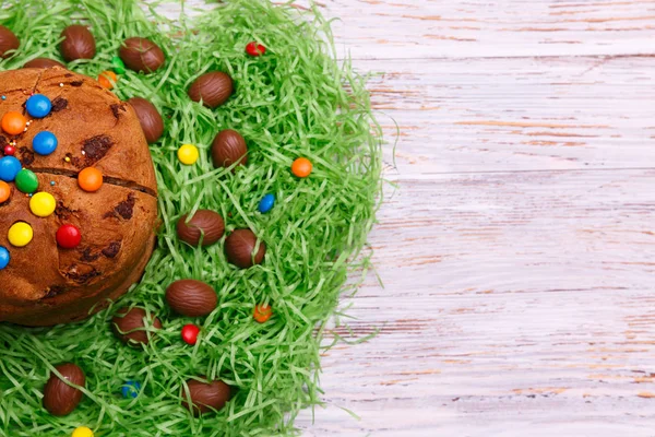 Easter Paska cake and chocolate eggs in green grass on a wooden background, top view. Traditional Easter bread with eggs.