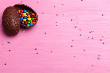 Çikolata Paskalya yumurtası ve parlak pembe ahşap arka plan üzerinde renkli şekerler. Paskalya kavramı.