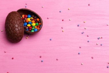 Çikolata Paskalya yumurtası ve parlak pembe bir arka plan üzerinde renkli şekerler. Paskalya tatlı kavramı.