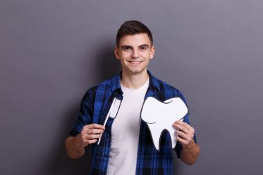 diş ve diş fırçası kağıt görüntüsü gri arka plan üzerinde tutan genç adam. Tıp ve diş hekimi kavramı ziyaret.