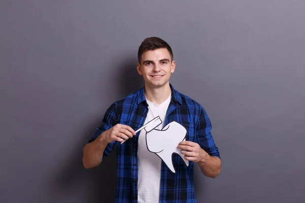 Молодий Чоловік Тримає Паперове Зображення Зуба Зубної Щітки Сірому Фоні — стокове фото