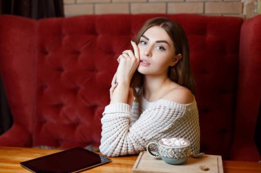 Kırmızı kanepede kafede kahve içme genç esmer güzel bir kadın. İçecekler ısınma konsepti.